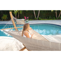 Woman relaxing poolside in a beige hammock with a drink