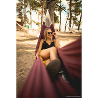 Woman sitting in a hammock on a beach with trees in the background