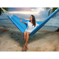 Woman relaxing in a blue hammock on a beach at sunset