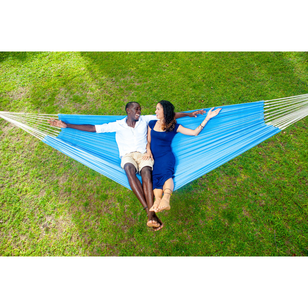 Two people relaxing in a blue hammock on a grassy field