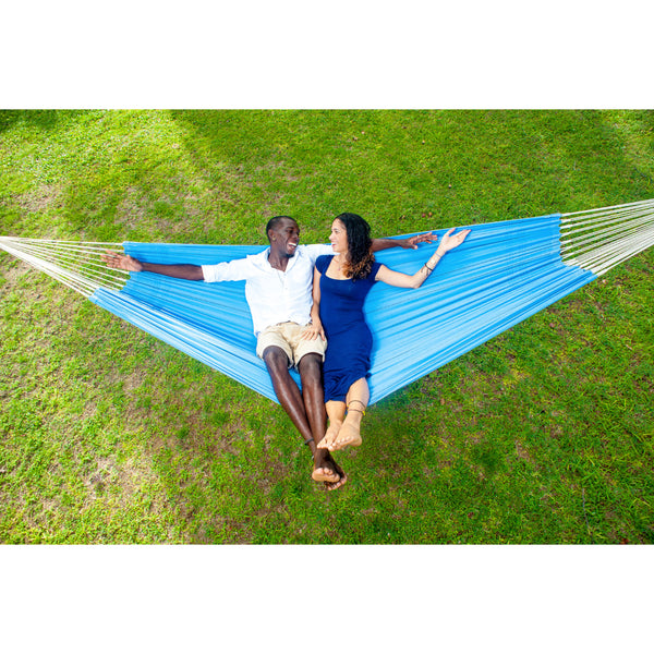 Two people relaxing in a blue hammock on a grassy field