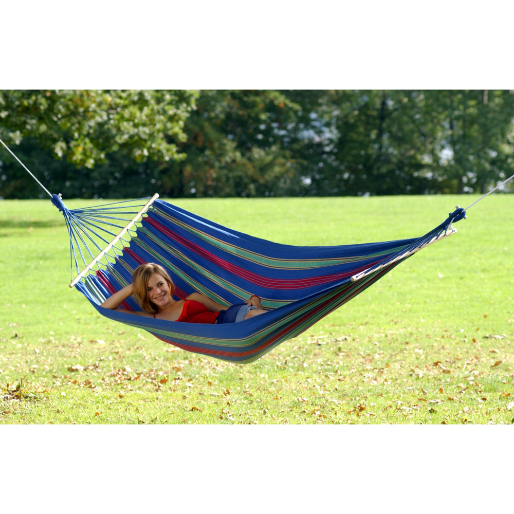 Person relaxing in a colorful striped hammock on a grassy field with trees in the background