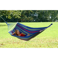 Person relaxing in a colorful striped hammock on a grassy field with trees in the background
