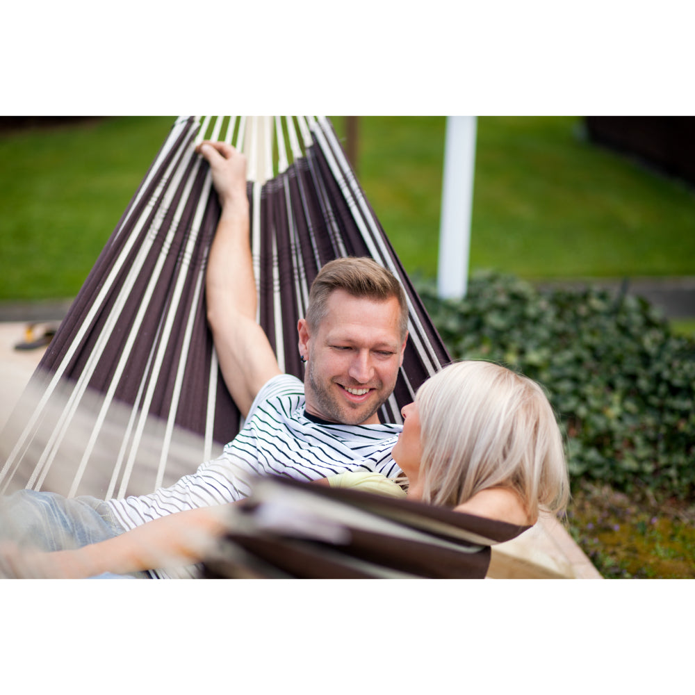 Man and woman relaxing in a striped hammock outdoors.