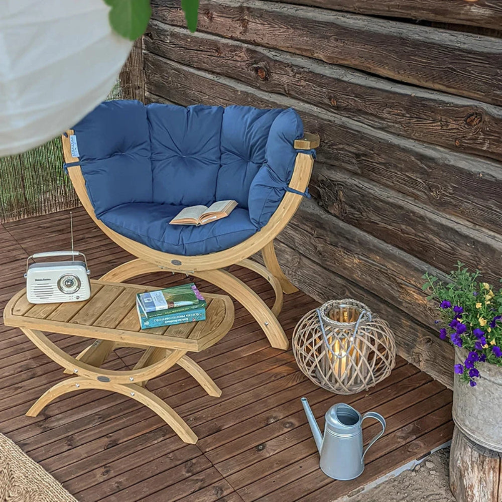 Wooden chair with blue cushion on a wooden deck, surrounded by books, a radio, and decorative items.