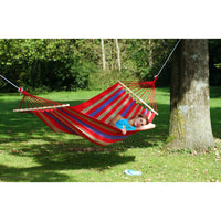 Person relaxing in a striped hammock under a tree in a park.