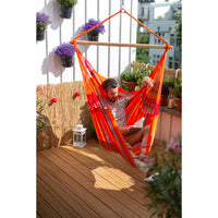Man reading book outside on balcony in brightly colour hammock chair