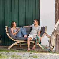 A man and a woman sitting on a modern outdoor chair with a mule in the background.