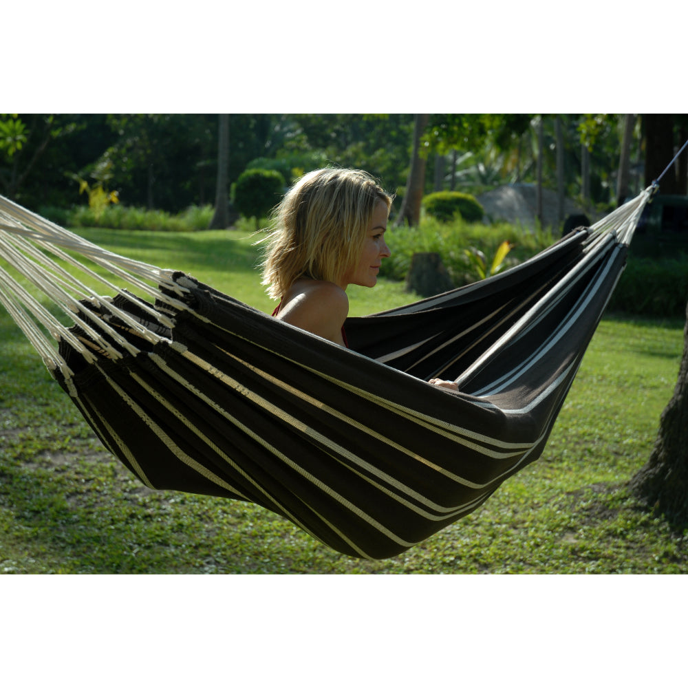 Woman sitting in a striped hammock in a garden setting