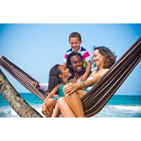 Family of four sitting in a hammock on a beach with clear blue sky and ocean.