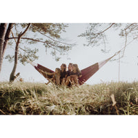 Three people sitting in a hammock between trees with a clear sky.