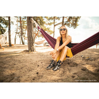Woman sitting in a hammock on a sandy beach with trees in the background