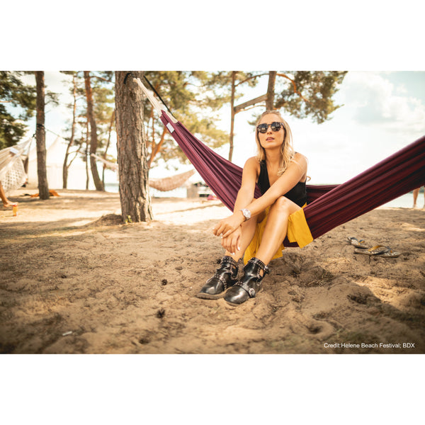 Woman sitting in a hammock on a sandy beach with trees in the background