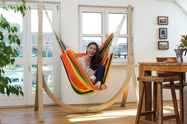 Woman sitting in a colorful hammock indoors with a wooden frame.