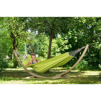 Person relaxing in a green hammock with a wooden stand in a park setting.