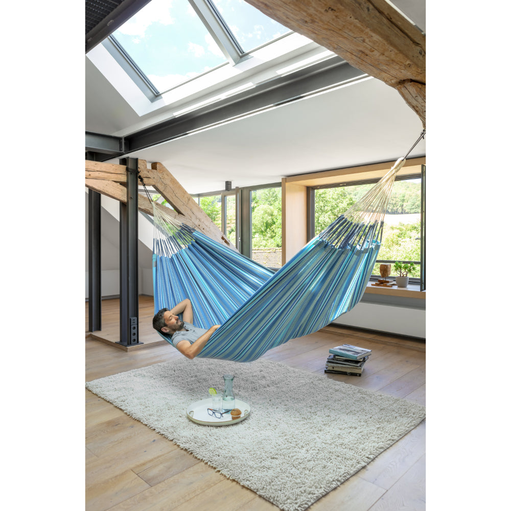 Man napping inside apartment in blue and white cotton hammock