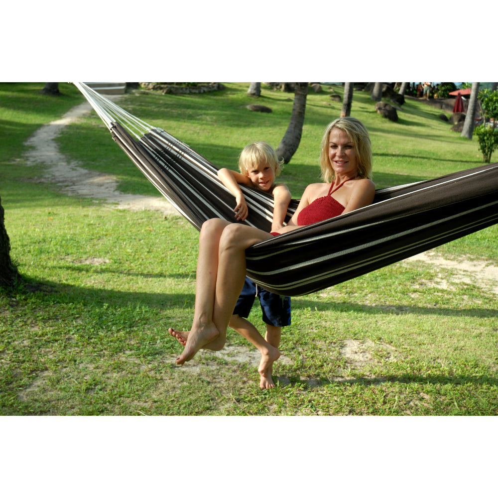 Woman and child in a striped hammock on a grassy area with trees.