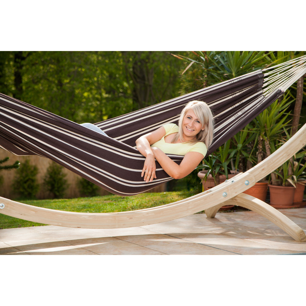 Woman relaxing in a striped hammock on a wooden stand with a garden background