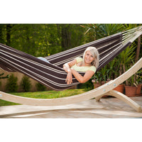 Woman relaxing in a striped hammock on a wooden stand with a garden background