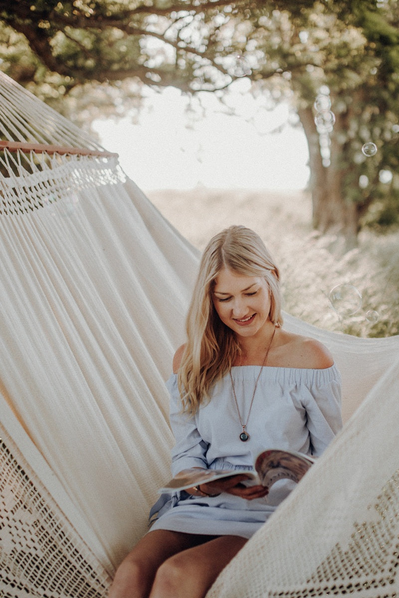 Woman reading a book in a white hammock under a tree