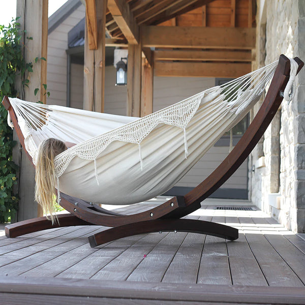 Woman sleeping in white fringed cotton hammock suspended from curved wooden hammock frame