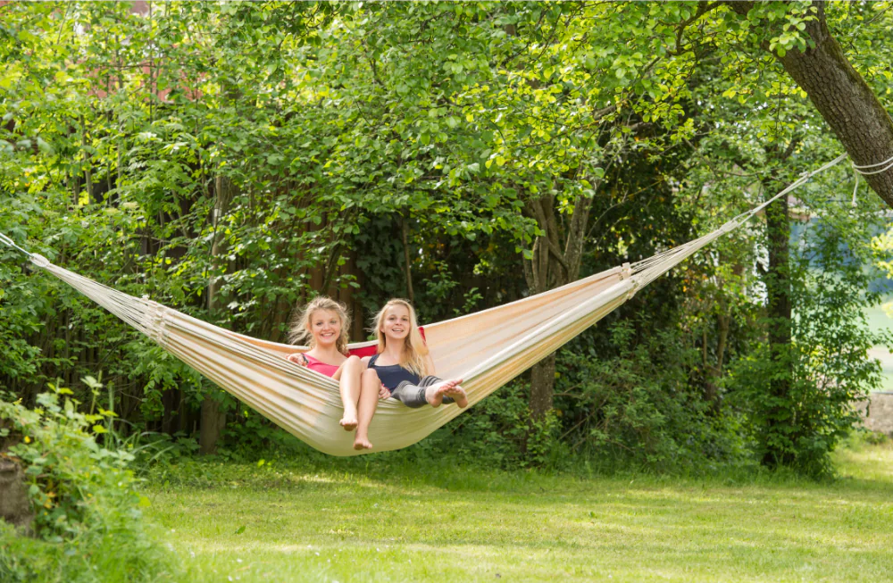 Two people sitting in a hammock in a park near a forest