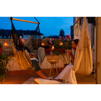 Man and woman enjoying a hot drink in hammock chairs under night lighting