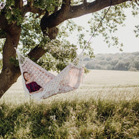 Person relaxing in a hammock under a tree in a field