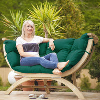 Woman sitting on a green cushioned outdoor chair with plants in the background