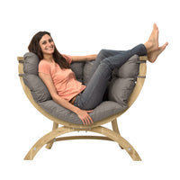 Woman sitting with legs up in a grey cushioned chair with wooden frame