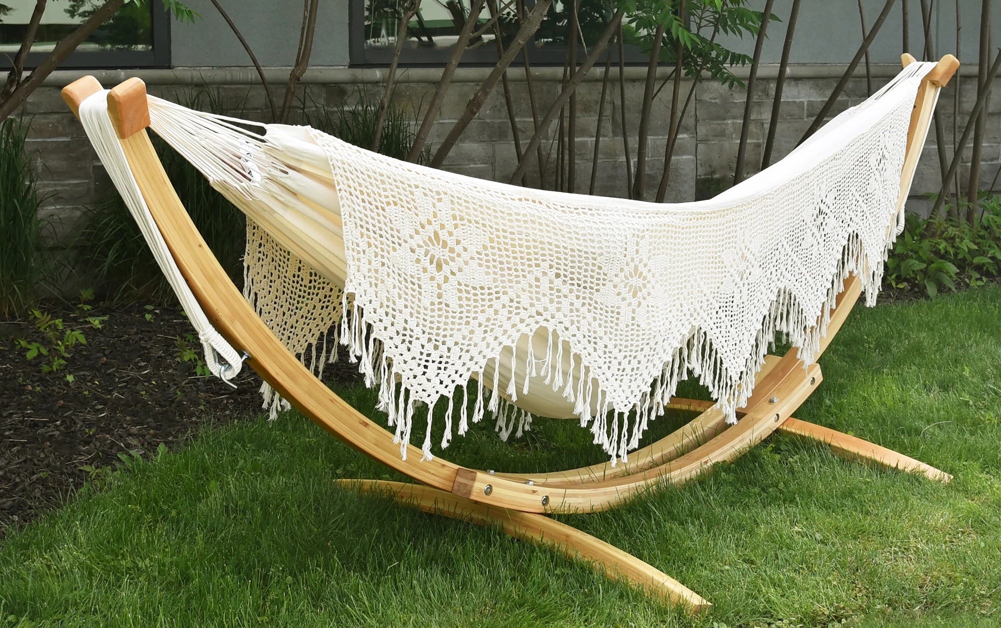 White crochet hammock on a wooden stand in a garden setting