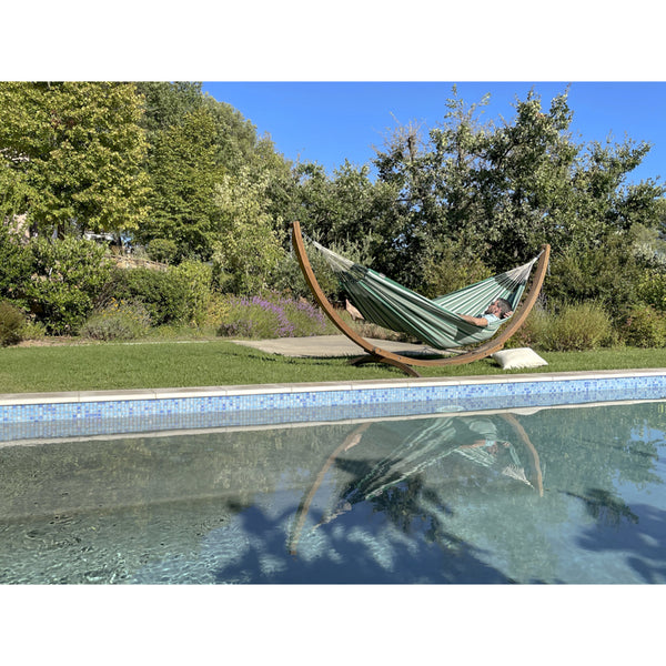 Man resting poolside in large wooden hammock frame